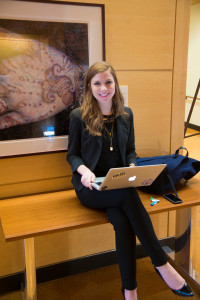Smiling, well-dressed Ross Business School student sits, legs crossed, with her laptop and phone.